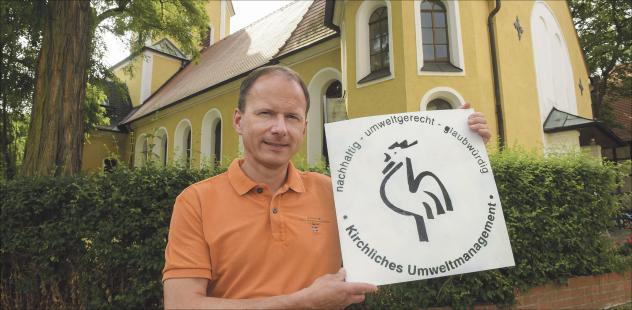 Auf dem Weg zum »Grünen Hahn«: Andreas Stötzner zeigt schon mal das Symbol für kirchlichen Umweltschutz vor seiner Laurentiuskirche in Leipzig-Leutzsch. Seit einem Jahr arbeitet er mit einer Umweltgruppe in der Kirchgemeinde an diesem Zertifikat, wofür er auch eine einjährige Ausbildung absolviert hat. Nächstes Jahr könnte sie den »Grünen Hahn« bekommen. Foto: Wolfgang Zeyen Grüner Hahn, Zertifikat, Laurentiuskirche, Leipzig-Leutzsch, Andreas Stötzner