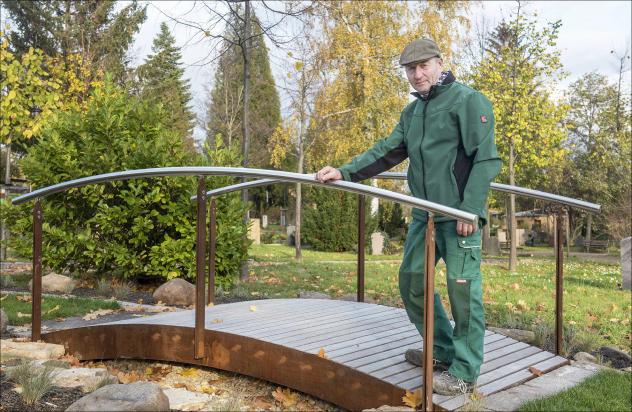 Friedhofsverwalter Hartmut Schneider steht auf einer Brücke des neuen Trauerwegs auf dem Friedhof in Dresden-Cotta. Schneider möchte damit Trauernde ansprechen sowie zum Spaziergang auf dem Friedhof einladen. Foto: Dietrich Flechtner