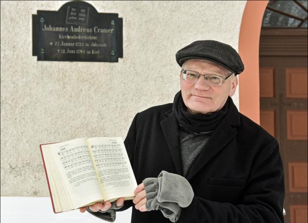 Kirchenmusiker Andreas Rockstroh erinnert am Haupteingang der St. Salvatorkirche an den Theologen Cramer, der in Jöhstadt geboren wurde. Eine Tafel mit Gesangbuch »Der Herr ist Gott, und keiner mehr« und Lebensdaten sind zu sehen. Foto: privat