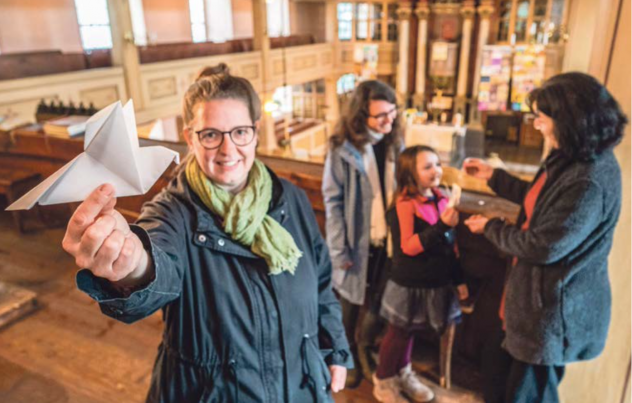 Ausgefallene Kunstprojekte in der Kirche Wildbach: Künstlerin Annett Beier hält eine gebastelte Friedenstaube in der Hand, im Hintergrund Pfarrerin Dominique Meichsner mit Tochter Noa und Diakonin Katrin Kauk.