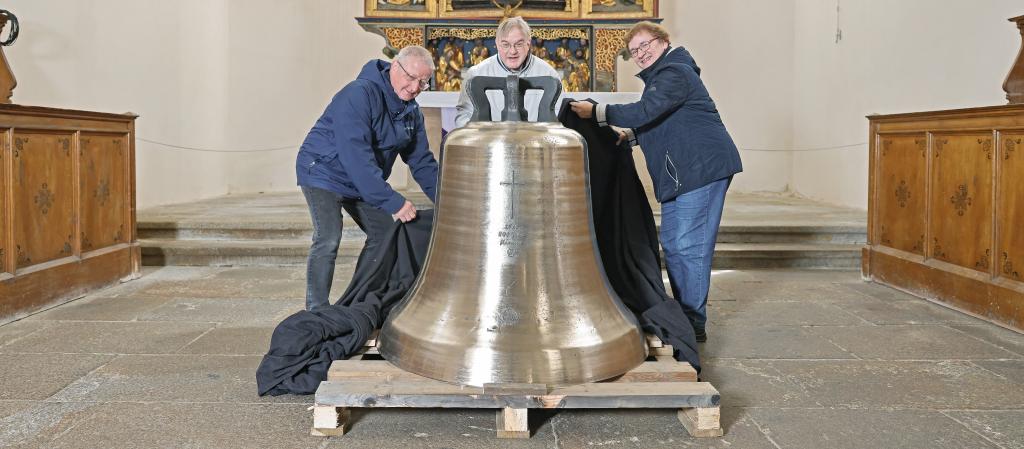 Pfarrer Joachim Krönert (li.) sowie Angelika und Michael Pöche lüften schon einmal die Abdeckung der neuen Kamenzer Glocke. Noch lagert das Schwergewicht in der Klosterkirche/Sakralmuseum St. Annen. © Dirk Sukow