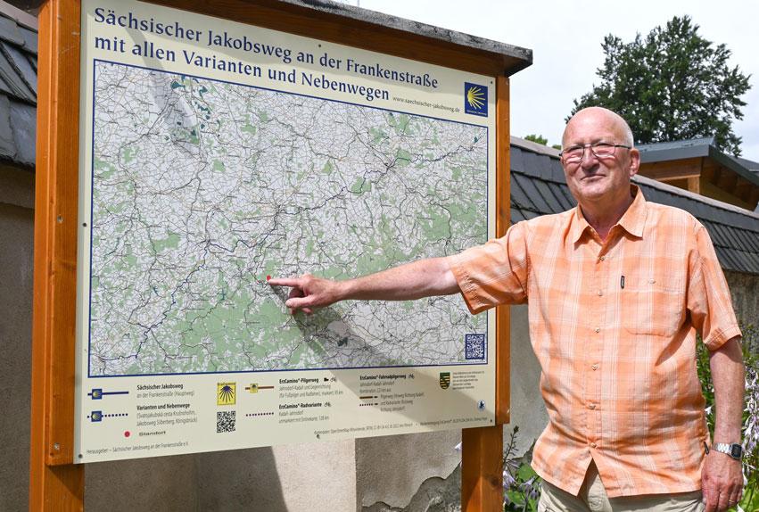 Vor der Kirche steht die neue Infotafel zum Sächsischen Jakobsweg: Ulrich Kästli zeigt den Standort Elterlein. Auch eine Stempelstelle gibt’s gleich neben dem Pfarrhaus. © Christine Bergmann 