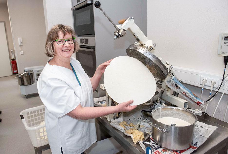 Carola Schmiedt in der Hostienbäckerei: Sie stellt Hostien aus dickflüssigem Teig aus Weizenmehl und Wasser her. Raumhohe Scheiben und eine Tür aus Glas trennen den Verkaufsraum von der Bäckerei. © Dietrich Flechtner 