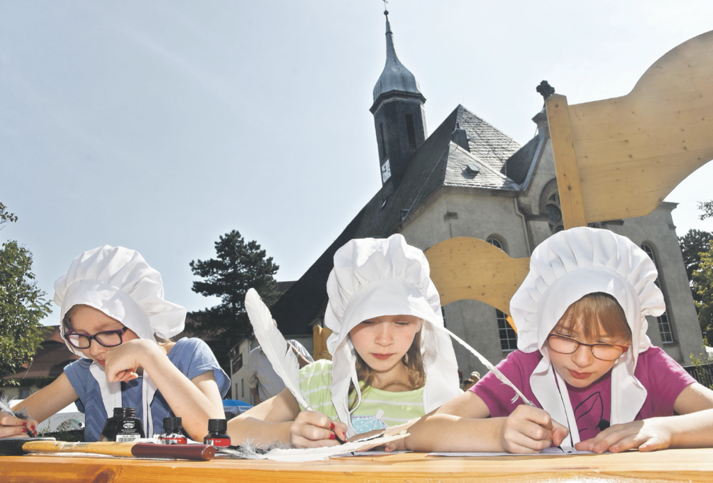 Schreiben wie zu Luthers Zeiten beim »Tag der Sachsen« 2016: Die Mädchen Jida, Gesa und Nea arbeiten voll konzentriert auf dem Gelände der Limbacher Stadtkirche. © Steffen Giersch