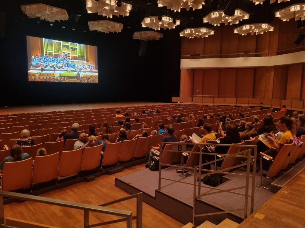 Da der große Saal voll ist, wird auch nebenan per Videoschalte mitgeprobt © Karola Richter Gemeinsames Einsingen © Karola Richter