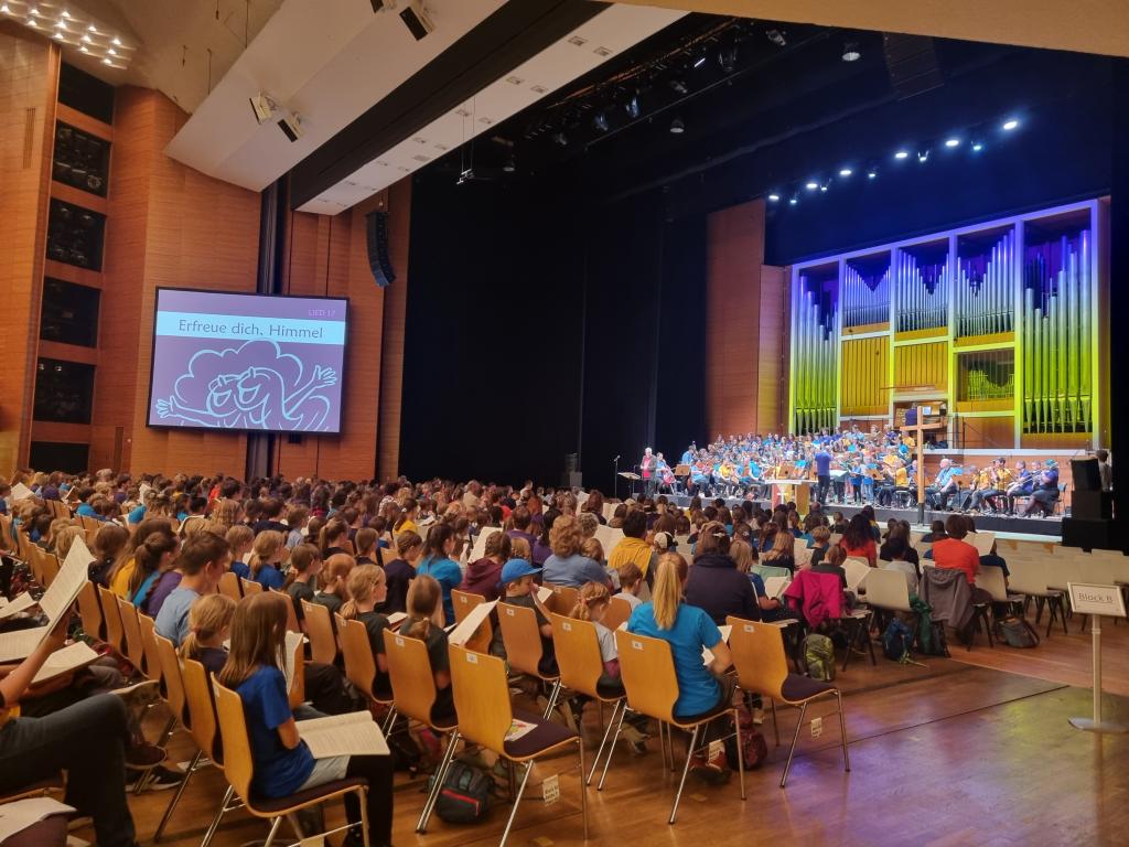 Im Saal werden am Vormittag die Lieder für das Musical 16 Uhr geprobt. Auf der Bühne im roten Shirt Ekkehard Hübler, Landesobmann des Kirchenchorwerks Sachsen © Karola Richter Gemeinsames Einsingen © Karola Richter