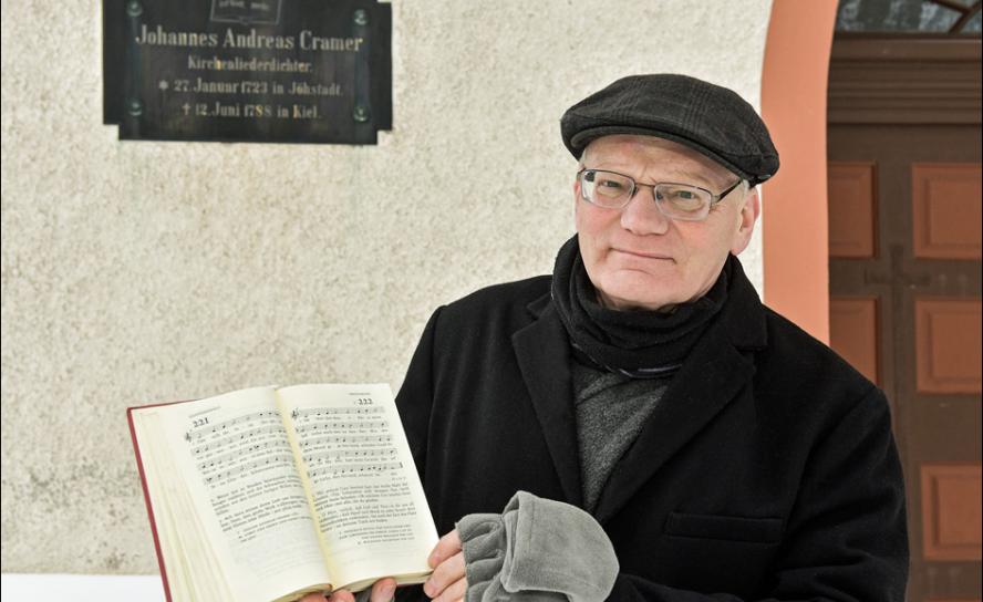 Kirchenmusiker Andreas Rockstroh erinnert am Haupteingang der St. Salvatorkirche an den Theologen Cramer, der in Jöhstadt geboren wurde. Eine Tafel mit Gesangbuch »Der Herr ist Gott, und keiner mehr« und Lebensdaten sind zu sehen. Foto: privat